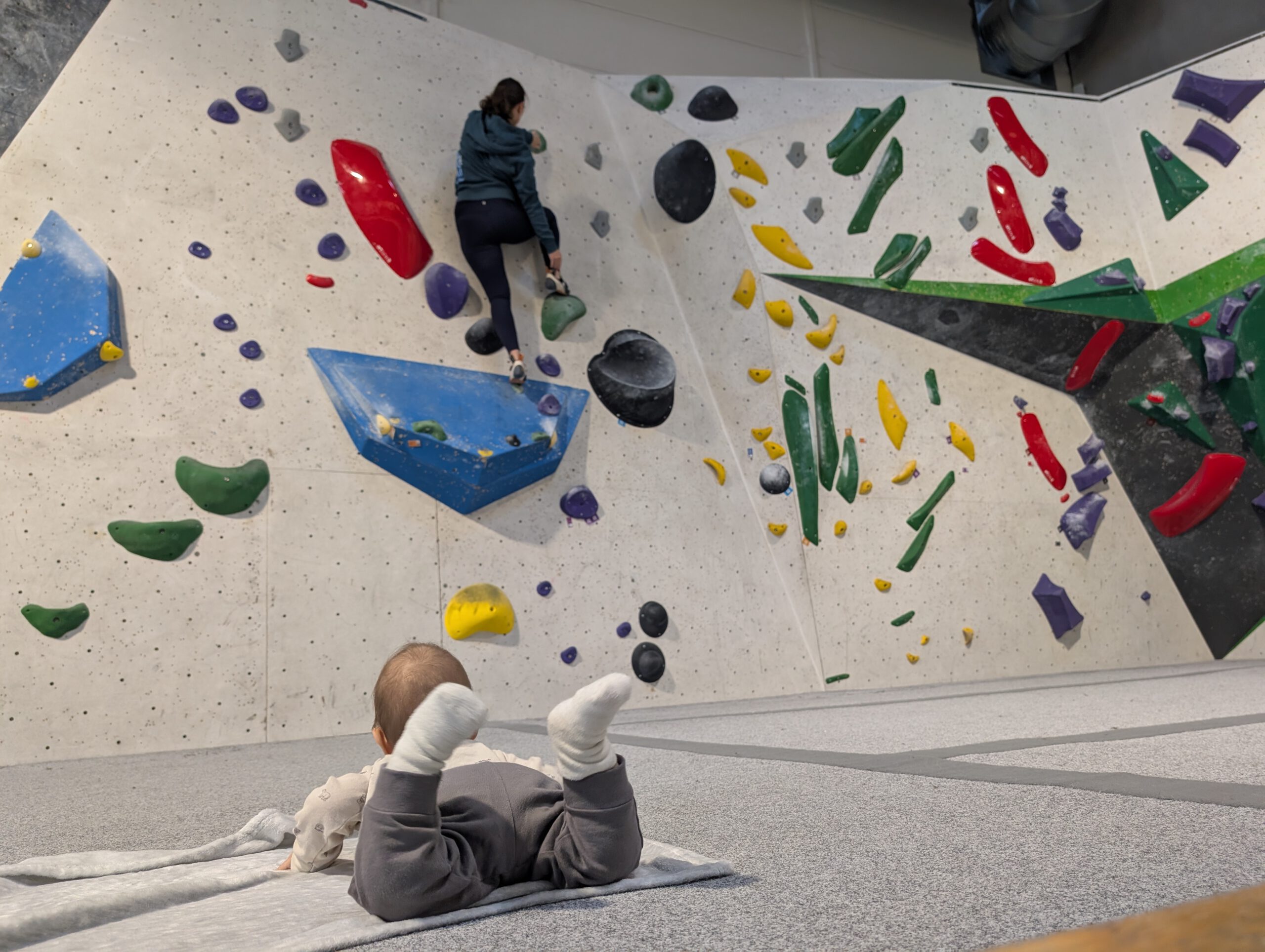 Mutter bouldert während Baby zuschaut